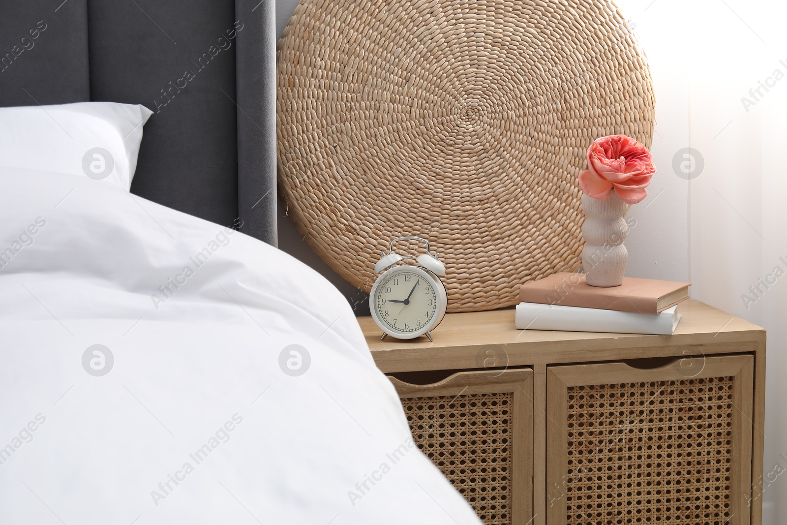 Bedside table with alarm clock, decor and books near bed indoors Photo of Bedside table with alarm clock, decor and books near bed indoors
