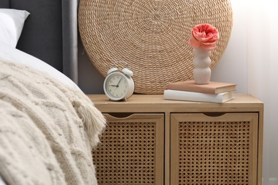Photo of Bedside table with alarm clock, decor and books near bed indoors