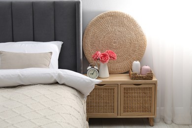 Photo of Bedside table with alarm clock and decor near bed indoors