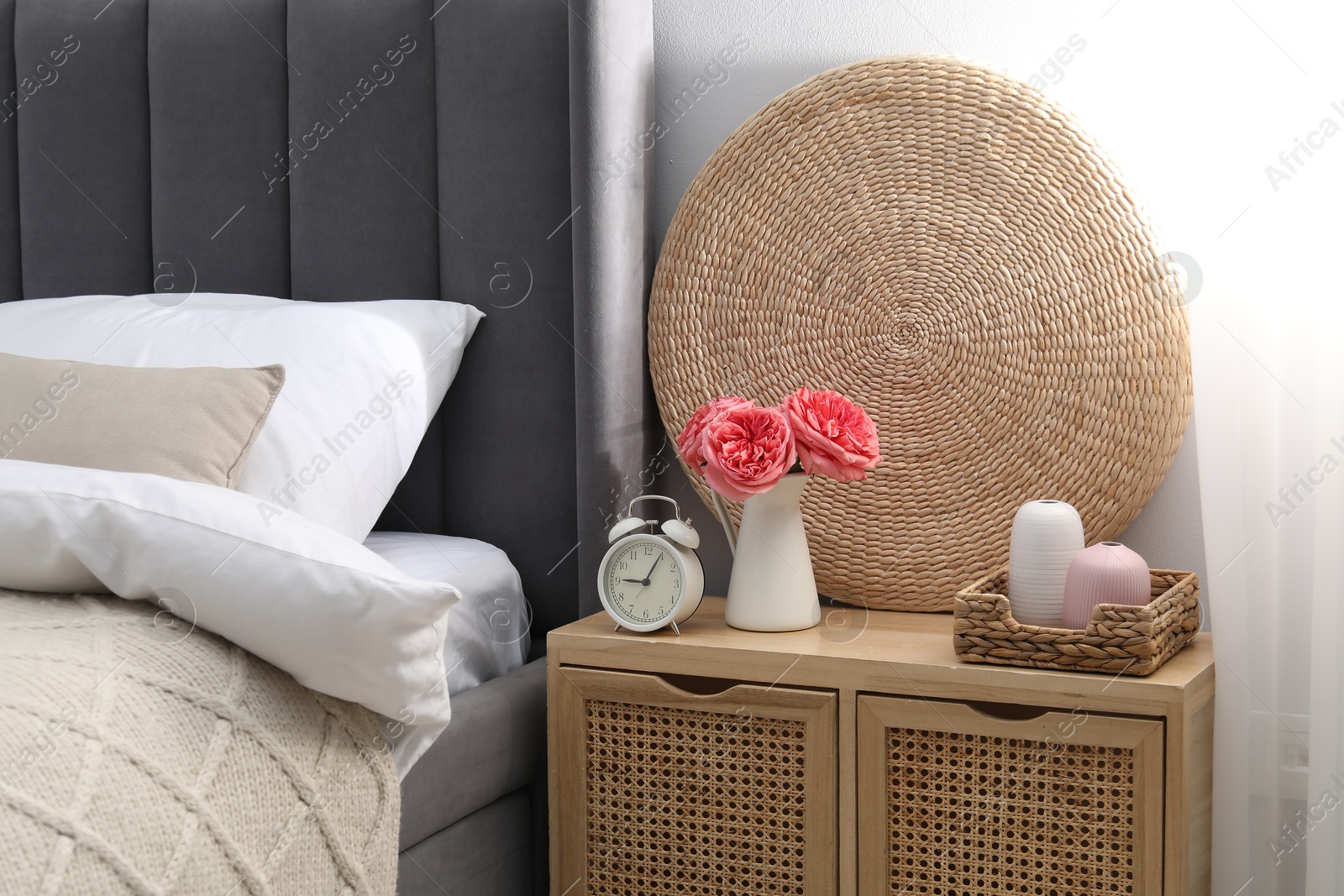 Bedside table with alarm clock and decor near bed indoors Photo of Bedside table with alarm clock and decor near bed indoors
