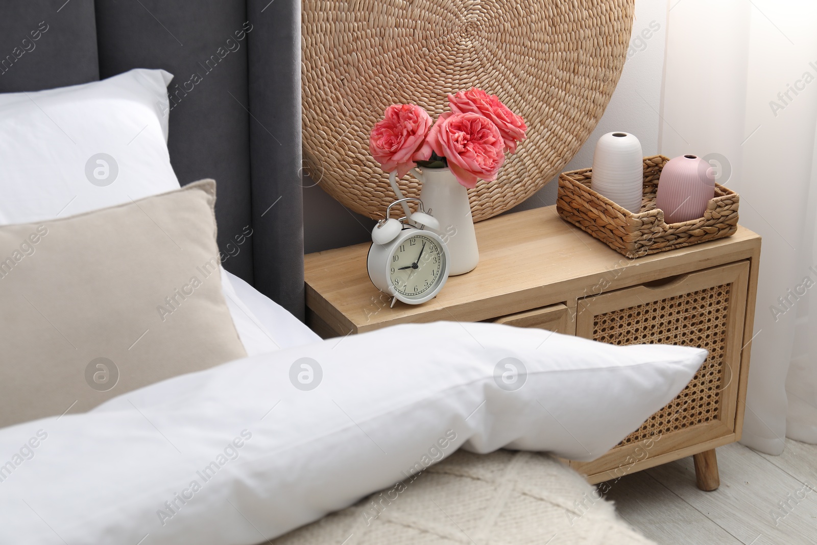 Bedside table with alarm clock and decor near bed indoors Photo of Bedside table with alarm clock and decor near bed indoors