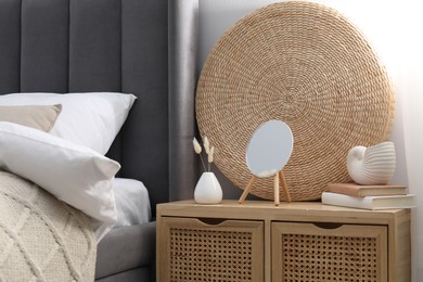 Photo of Bedside table with mirror, decor and books near bed indoors