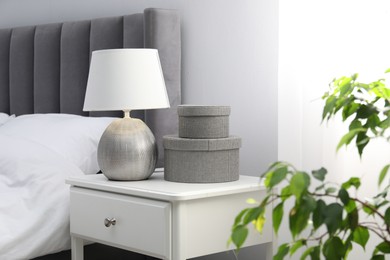 Photo of Bedside table with lamp and decor near bed indoors
