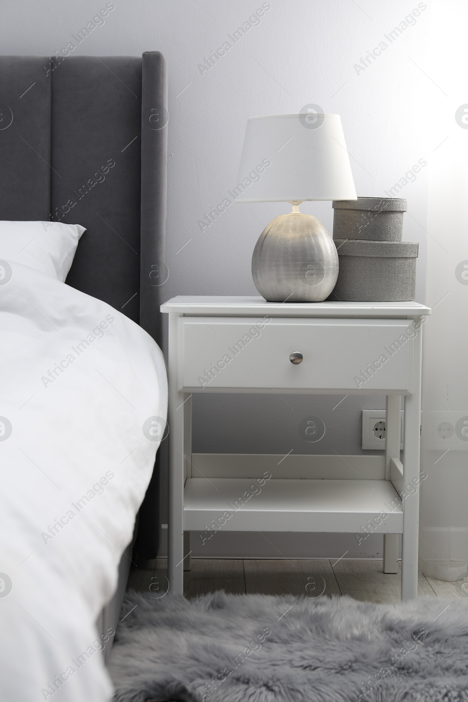 Bedside table with lamp and decor near bed indoors Photo of Bedside table with lamp and decor near bed indoors