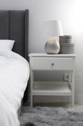 Photo of Bedside table with lamp and decor near bed indoors