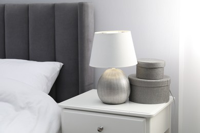 Photo of Bedside table with lamp and decor near bed indoors