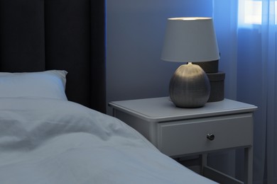 Photo of Bedside table with lamp and decor near bed indoors