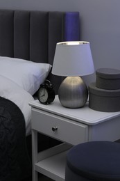 Photo of Bedside table with lamp, alarm clock and decor near bed indoors