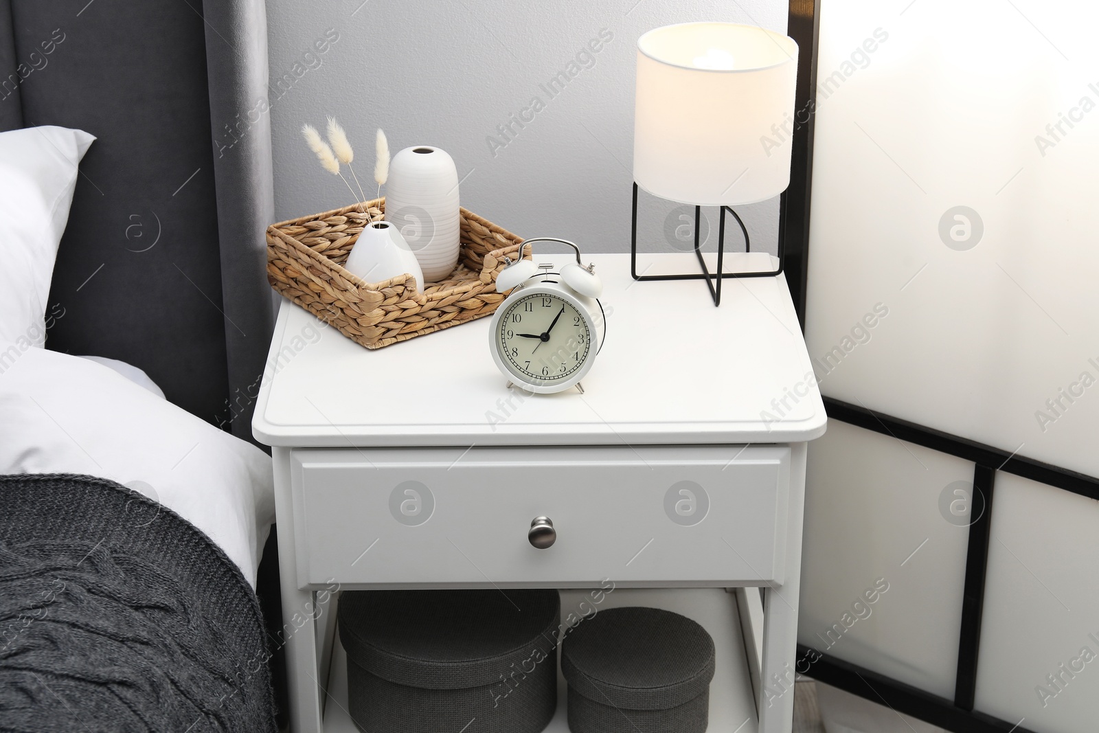Photo of Bedside table with lamp, alarm clock and decor near bed indoors