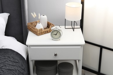 Photo of Bedside table with lamp, alarm clock and decor near bed indoors