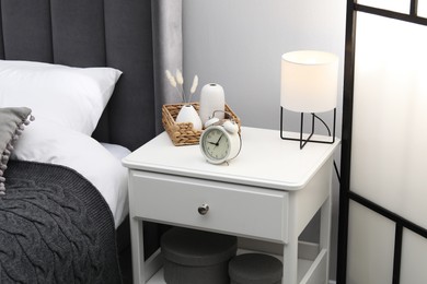 Photo of Bedside table with lamp, alarm clock and decor near bed indoors