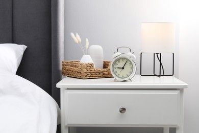 Photo of Bedside table with lamp, alarm clock and decor near bed indoors
