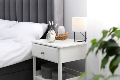 Photo of Bedside table with lamp, alarm clock and decor near bed indoors