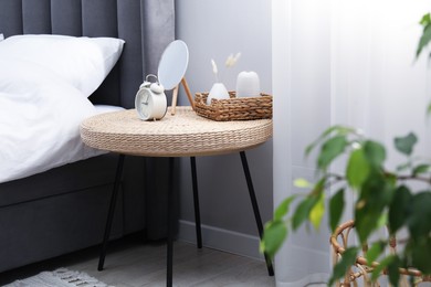 Photo of Side table with mirror, alarm clock and decor near bed indoors
