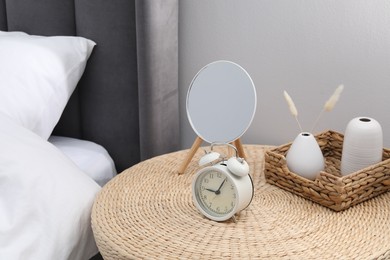 Photo of Side table with mirror, alarm clock and decor near bed indoors