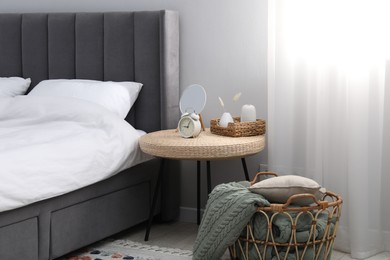 Photo of Side table with mirror, alarm clock and decor near bed indoors