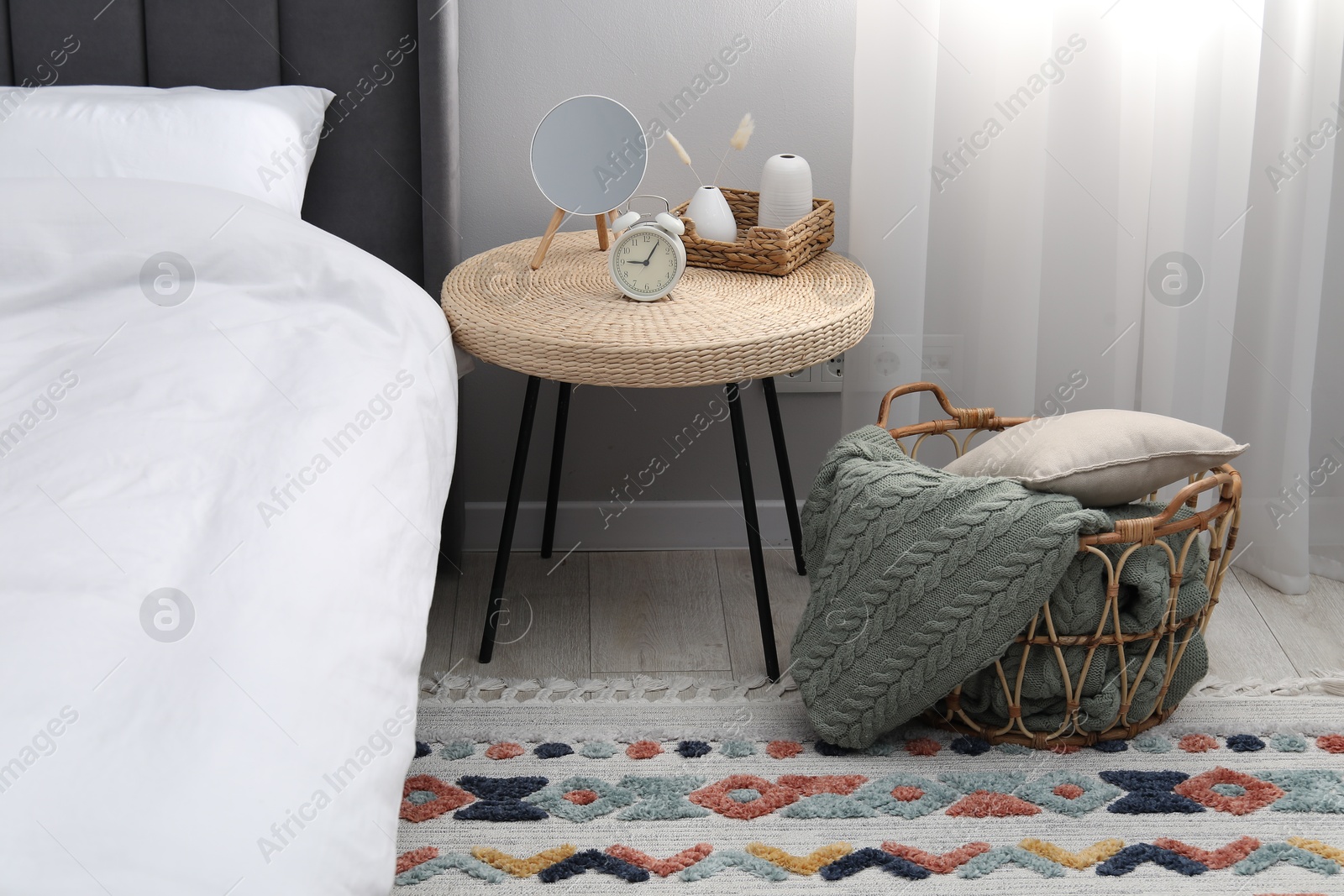 Side table with mirror, alarm clock and decor near bed indoors Photo of Side table with mirror, alarm clock and decor near bed indoors