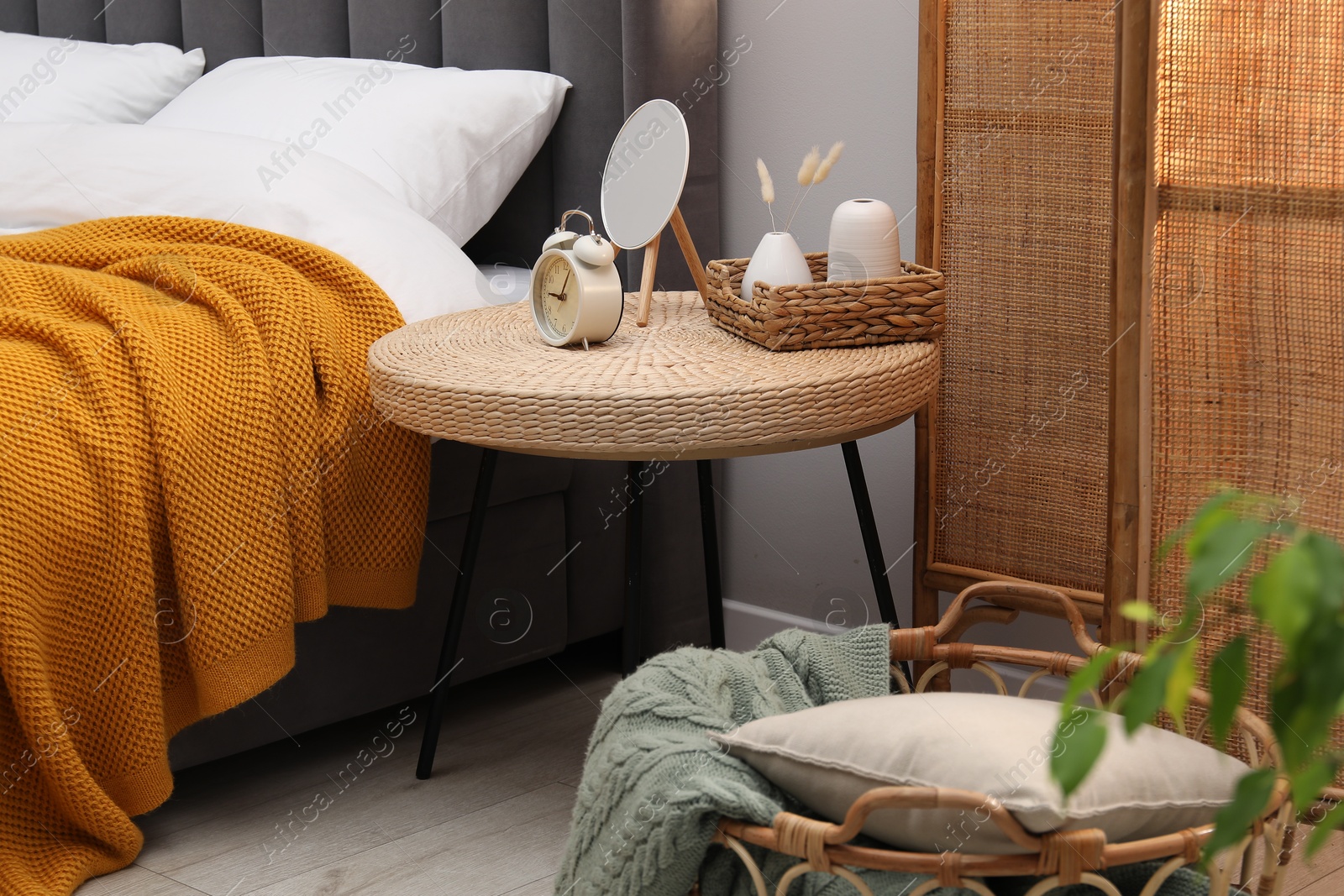 Side table with mirror, alarm clock and decor near bed indoors Photo of Side table with mirror, alarm clock and decor near bed indoors