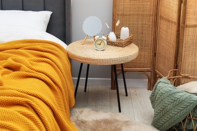 Photo of Side table with mirror, alarm clock and decor near bed indoors
