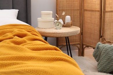 Photo of Side table with alarm clock and decor near bed indoors