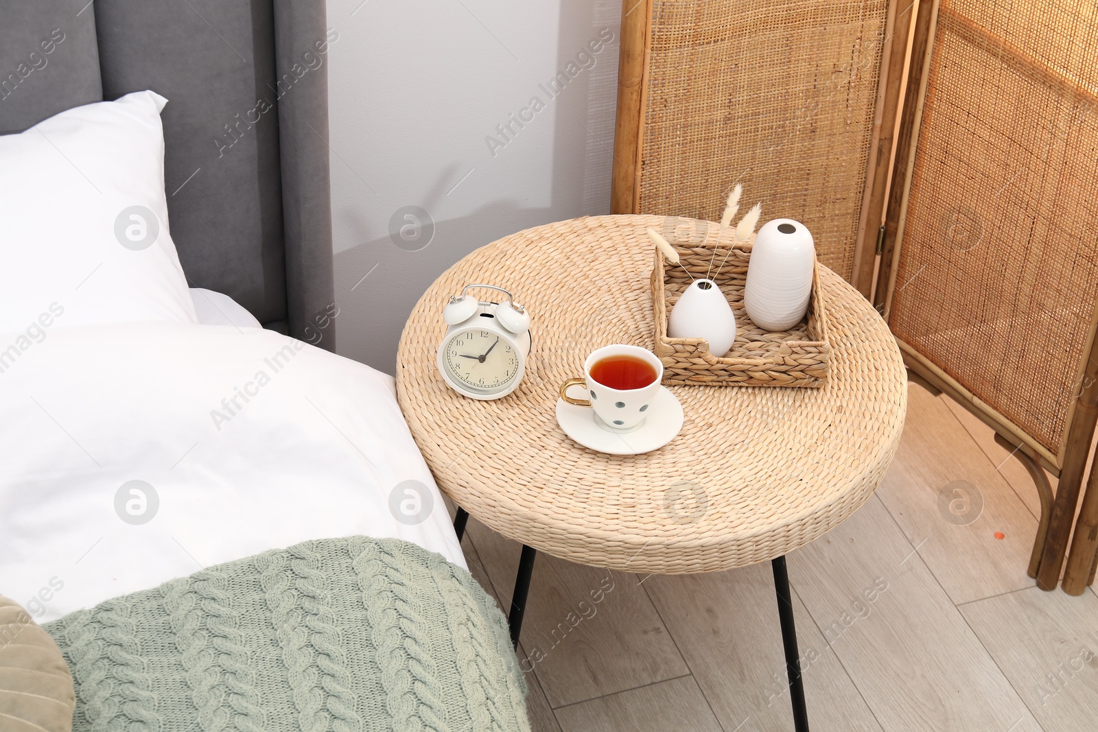 Side table with alarm clock, cup of tea and decor near bed indoors, above view Photo of Side table with alarm clock, cup of tea and decor near bed indoors, above view