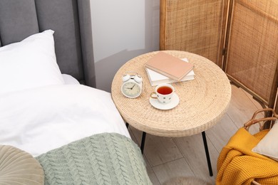 Photo of Side table with alarm clock, cup of tea and books near bed indoors, above view