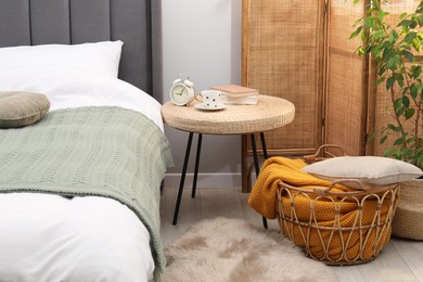Photo of Side table with alarm clock, cup of drink and decor near bed indoors