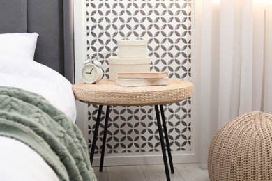 Photo of Side table with alarm clock, books and decor near bed indoors