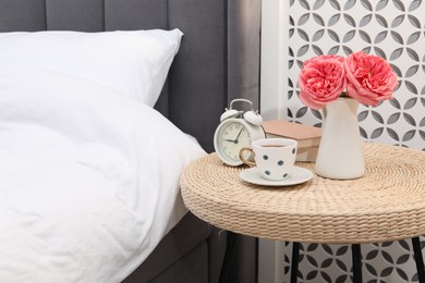 Photo of Side table with alarm clock, cup of tea, books and decor near bed indoors