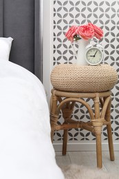 Photo of Side table with alarm clock and flowers near bed indoors