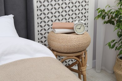 Photo of Side table with alarm clock and books near bed indoors