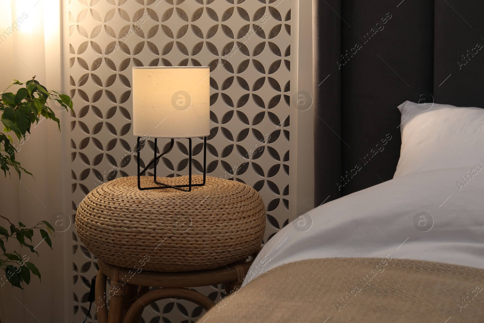 Side table with lamp near bed indoors Photo of Side table with lamp near bed indoors