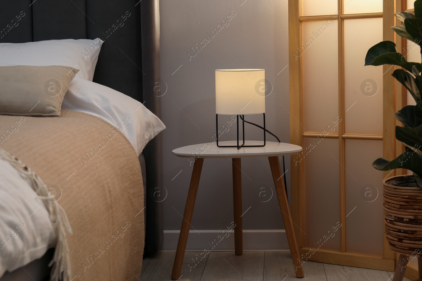 Side table with lamp near bed indoors Photo of Side table with lamp near bed indoors