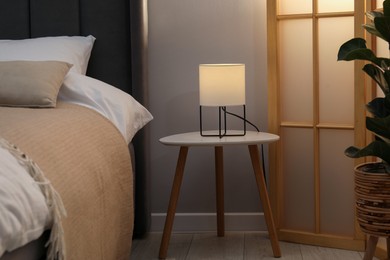 Photo of Side table with lamp near bed indoors