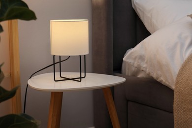 Photo of Side table with lamp near bed indoors