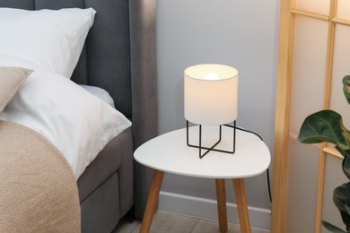 Photo of Side table with lamp near bed indoors