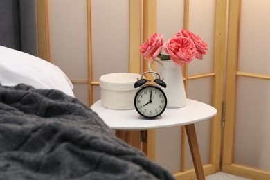 Photo of Side table with alarm clock and decor near bed indoors