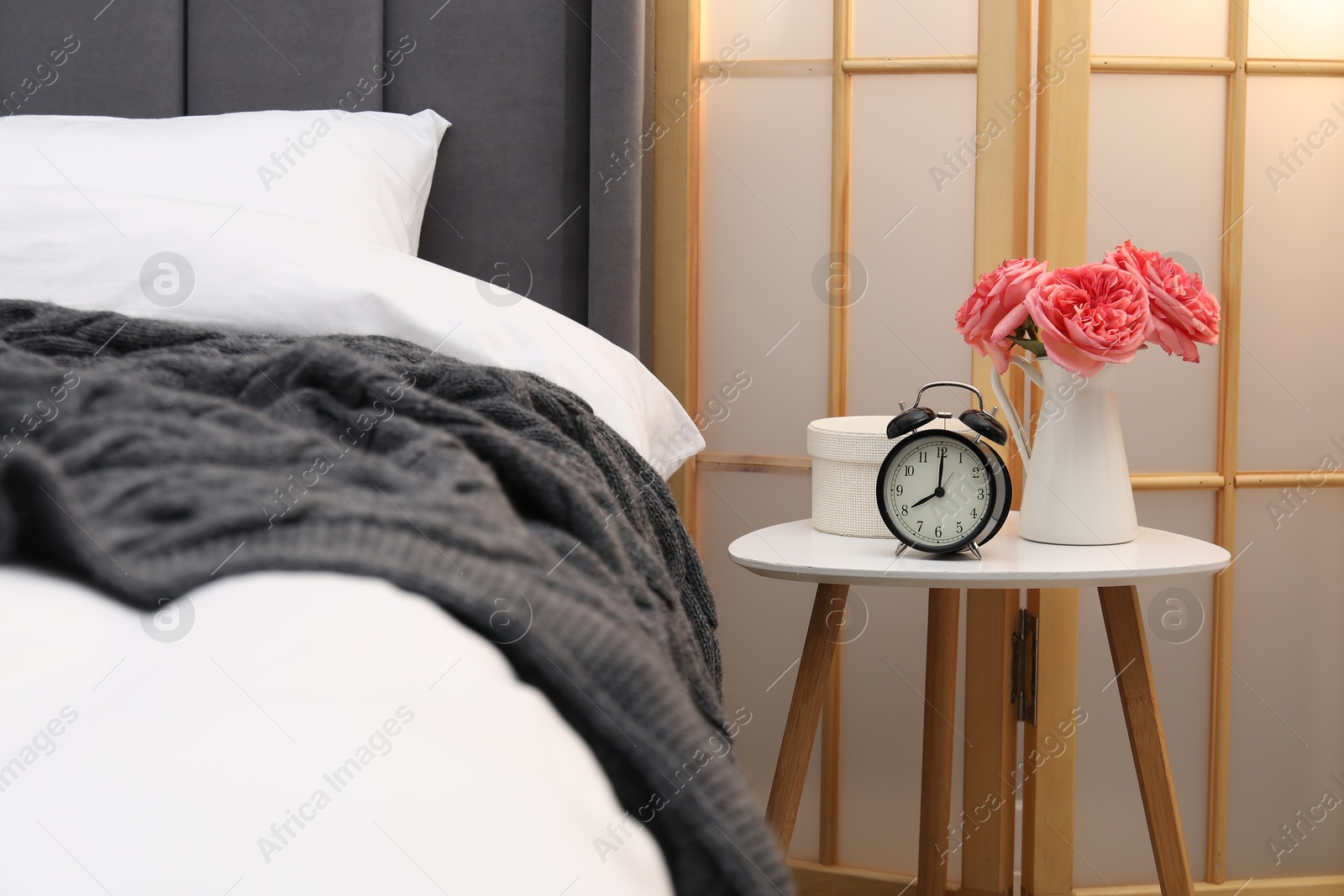 Side table with alarm clock and decor near bed indoors Photo of Side table with alarm clock and decor near bed indoors