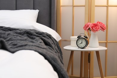 Photo of Side table with alarm clock and decor near bed indoors