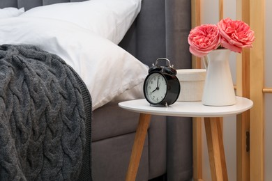 Photo of Side table with alarm clock and decor near bed indoors