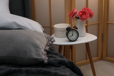 Photo of Side table with alarm clock and decor near bed indoors