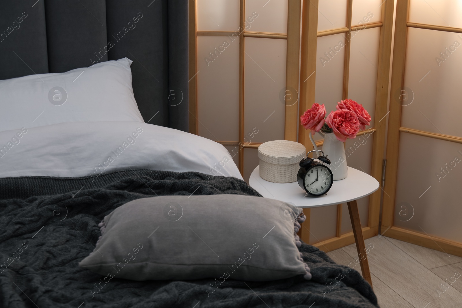 Side table with alarm clock and decor near bed indoors Photo of Side table with alarm clock and decor near bed indoors