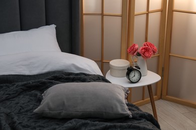 Photo of Side table with alarm clock and decor near bed indoors