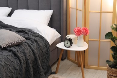 Photo of Side table with alarm clock and decor near bed indoors