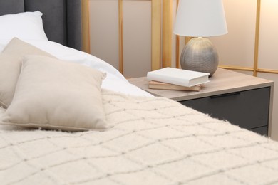 Photo of Bedside table with lamp and books near bed indoors