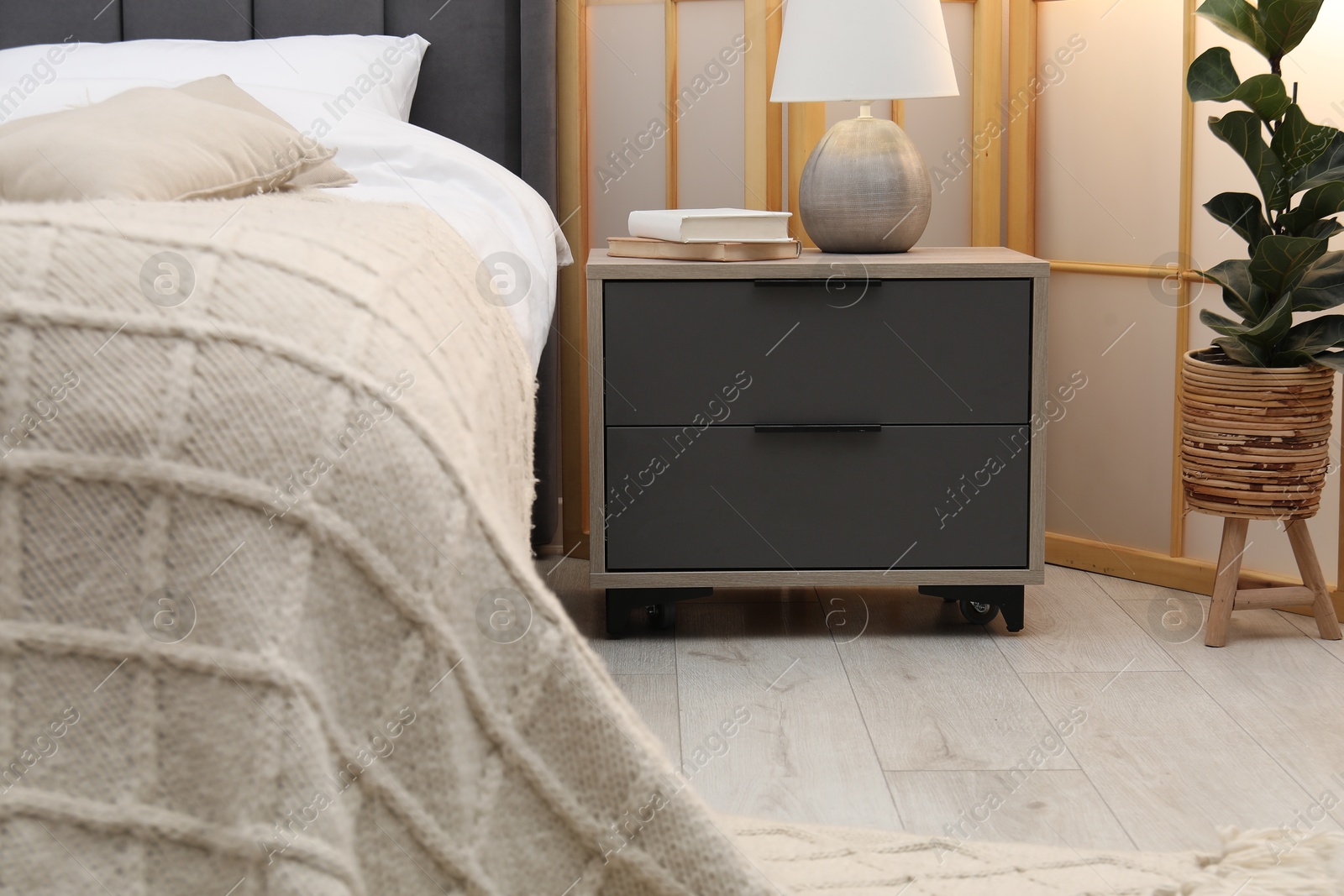Bedside table with lamp and books near bed indoors Photo of Bedside table with lamp and books near bed indoors