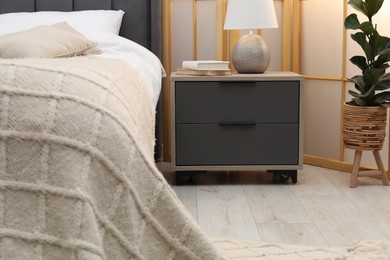 Photo of Bedside table with lamp and books near bed indoors