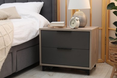 Photo of Bedside table with lamp, alarm clock and books near bed indoors