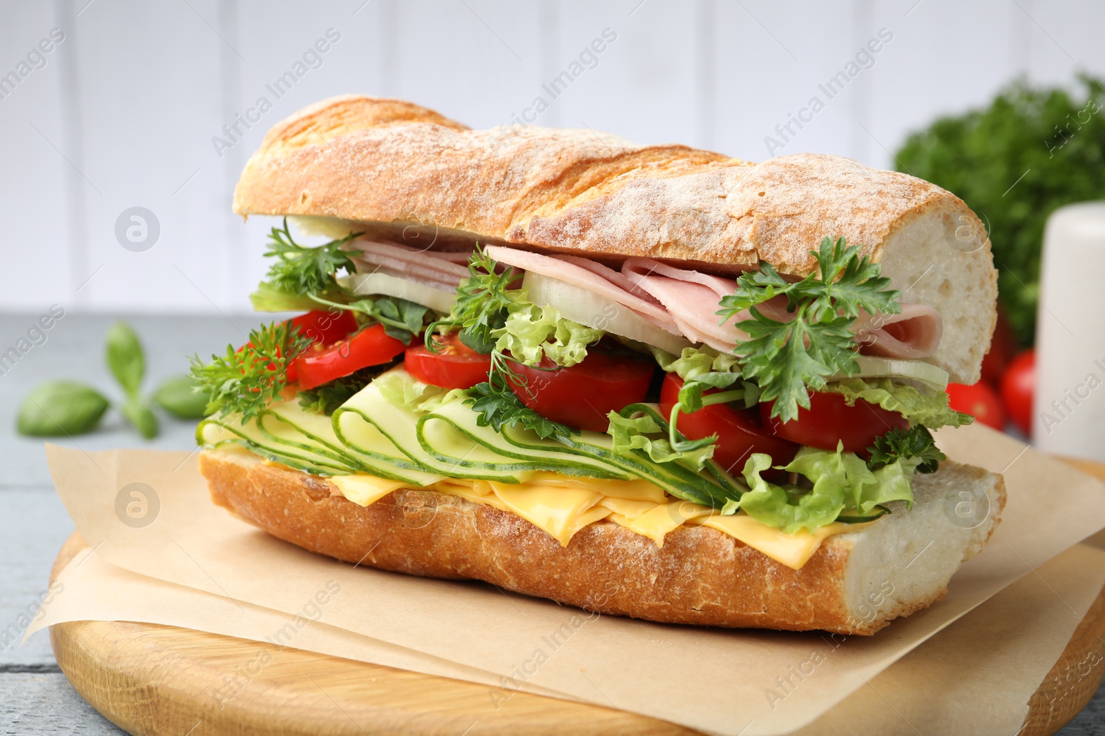 Tasty baguette sandwich with ham, cheese and vegetables on wooden table against grey background, closeup Photo of Tasty baguette sandwich with ham, cheese and vegetables on wooden table against grey background, closeup