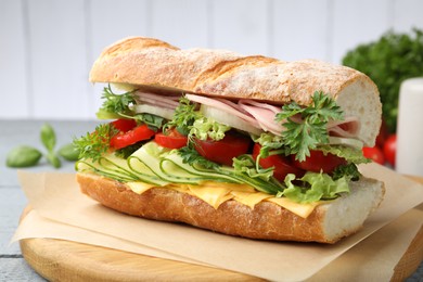 Photo of Tasty baguette sandwich with ham, cheese and vegetables on wooden table against grey background, closeup